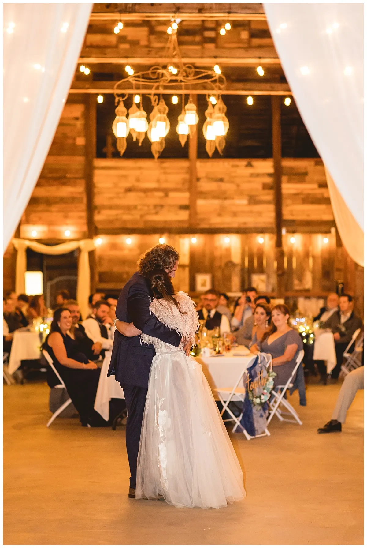 Guests dancing inside the rustic reception barn lit with warm string lights